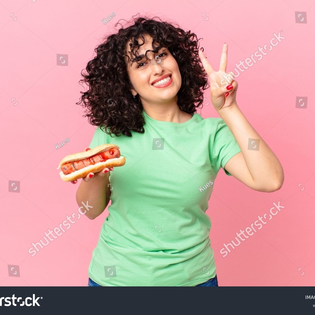 stock-photo-pretty-arab-woman-smiling-and-looking-friendly-showing-number-two-and-holding-a-hot-dog-2198409405